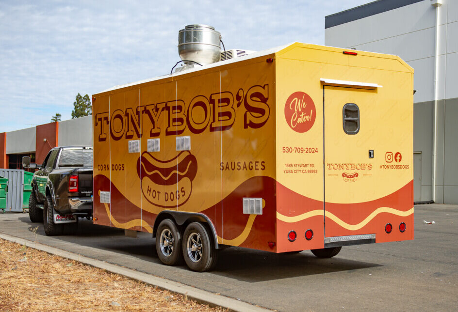 Complete vehicle wrap in muted mustard yellow with bold brown lettering and hotdog graphics.