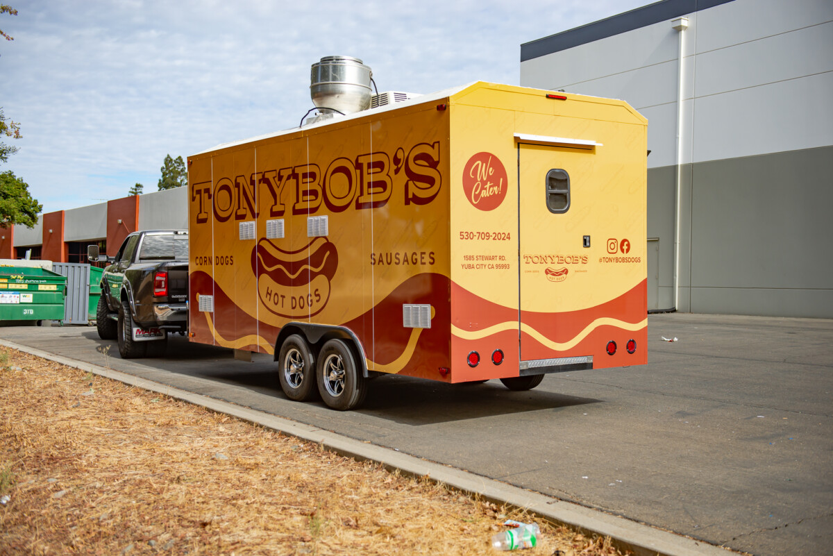 Complete vehicle wrap in muted mustard yellow with bold brown lettering and hotdog graphics.