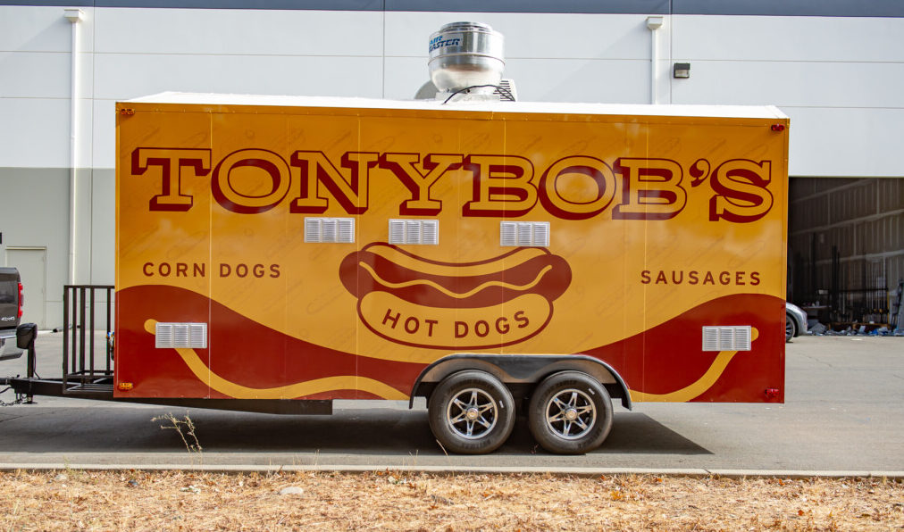 Food truck in a full mustard-yellow and brown wrap featuring Tony Bob's Hotdogs logo.